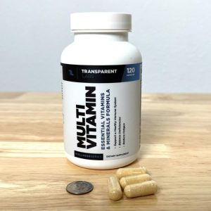 bottle of transparent labs multivitamin with capsules next to dime for size comparison