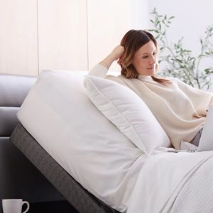 A woman sits on her bed frame on her laptop.