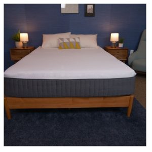 A bed with a dark gray mattress featuring a white top surface, set in a bedroom with a blue wall, wooden nightstands with lamps, and a framed picture above the bed.