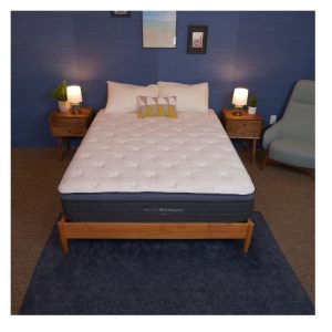 A bed with a dark gray mattress featuring a white quilted top, set in a bedroom with a blue wall, wooden nightstands with lamps, and a framed picture above the bed.