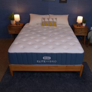 A Bear Elite Hybrid mattress on a wooden bed frame in a blue-themed bedroom with nightstands and lamps.