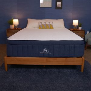 A Brooklyn Bedding mattress on a wooden bed frame with a blue-themed bedroom, featuring nightstands and lamps.