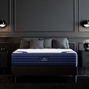 A DreamCloud mattress on a bed frame in a dark-themed bedroom with black walls and modern lighting fixtures.