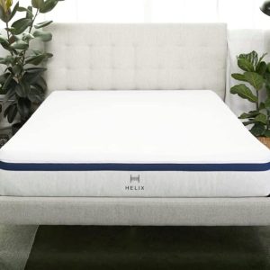 A Helix mattress on a bed frame with a tufted headboard, flanked by plants on either side.