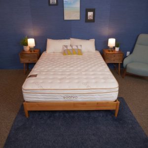 A Saatva mattress on a wooden bed frame with nightstands on either side, decorated with lamps and wall art.