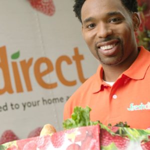 A man is smiling while holding a box of produce.