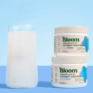 A glass of milk on the left side and two containers of Bloom Colostrum.