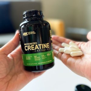 an open bottle of optimum nutrition creatine capsules in the hand of a professional product tester who is also holding several capsules in one hand to show capsule size