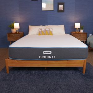 Bear Original mattress on a wooden bed frame, with a grey base and white top, in a simple and stylish bedroom.