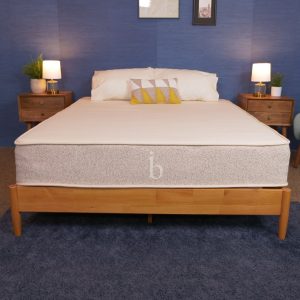 Birch Natural mattress on a wooden bed frame, with a light grey base and white top, set in a warm, inviting bedroom.