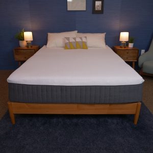 Emma Hybrid Comfort mattress in a simple, modern bedroom, with a white surface and gray sides, set on a wooden bed frame.