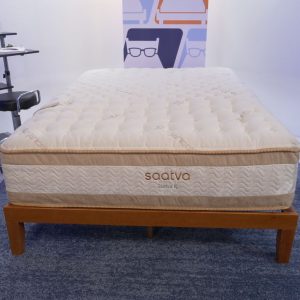 Saatva RX mattress on a wooden bed frame in a minimalist bedroom setting with soft lighting.