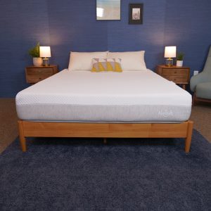 A bed with a white mattress set in a bedroom with a navy blue wall and two wooden nightstands with lamps. The bed is neatly made with pillows.