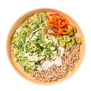 A healthy, vibrant bowl from Purple Carrot featuring a mix of farro, sliced olives, shredded Brussels sprouts, and colorful sliced peppers, all topped with a creamy green dressing.