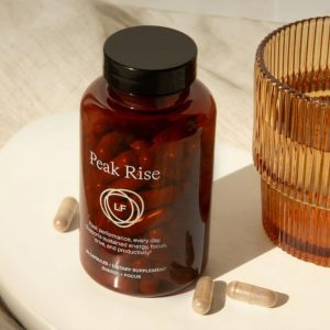 A bottle of Peak Rise Nootropics by a cup of water.