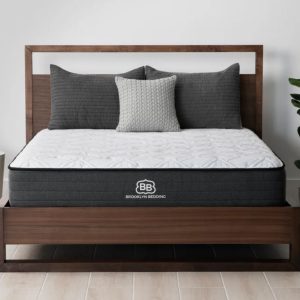 A Brooklyn Bedding Essential mattress on a wooden bed frame, with a cozy, modern bedroom setup.