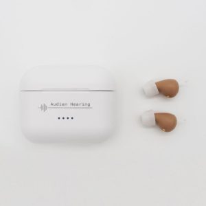 Pair of Audien Hearing aids next to branded white charging case