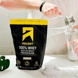 Tester pouring water next to a package of Ascent Whey Protein Vanilla Bean