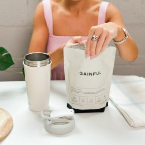 A person opening unflavored Gainful Protein Powder bag next to a shaker bottle