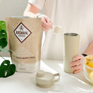 A person pouring a scoop of Vanilla Ka’Chava The Whole Body Meal into a shaker bottle