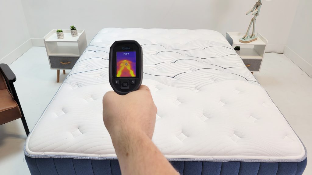 Tester holding a thermal imaging device aimed at a mattress, displaying a heat map on the screen