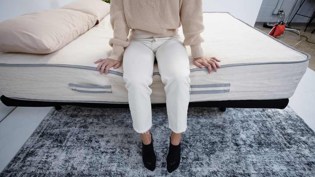 Tester sitting on the edge of a mattress with both hands resting on either side, testing the mattress's edge support