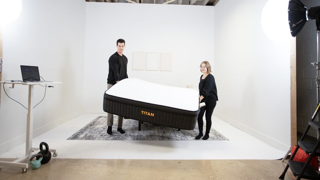 Two testers lifting a Titan mattress in a bright studio setup