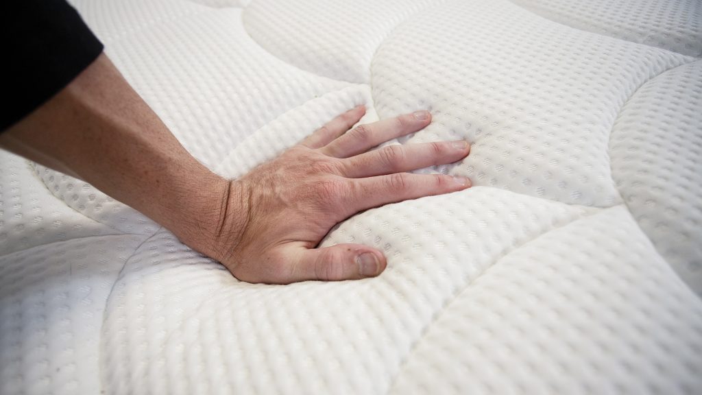 Close-up of a hand pressing down on a mattress surface, showing its plush texture and responsiveness