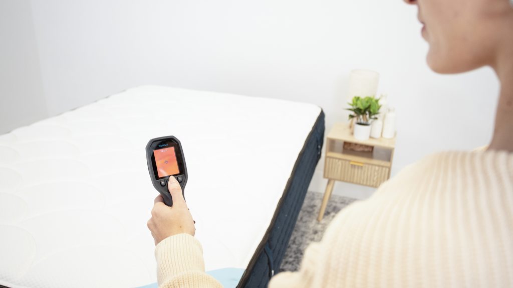 Tester holding a thermal imaging device aimed at a mattress to measure its surface temperature