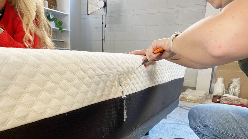 A tester cutting into the side of a mattress with a knife